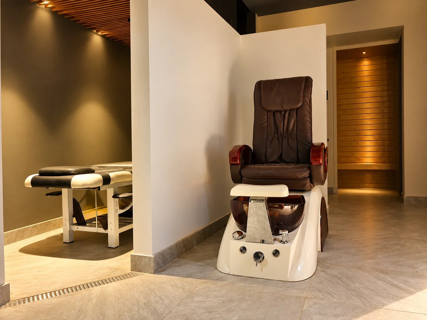A pedicure chair and massage table in a calm, warmly lit spa room